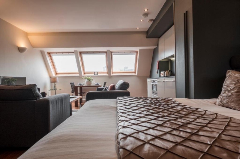 Modern szállodai stúdió franciaággyal, ülősarokkal, étkezőasztallal, tetőablakkal és kompakt konyhasarokkal, modern belső térrel.