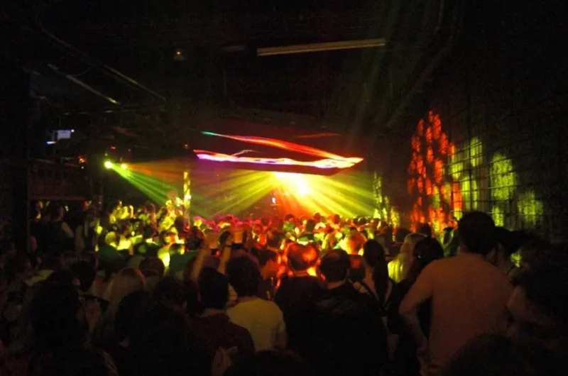 Zsúfolt táncparkett a bécsi Flex éjszakai klubban színes fényekkel és élő bulihangulattal