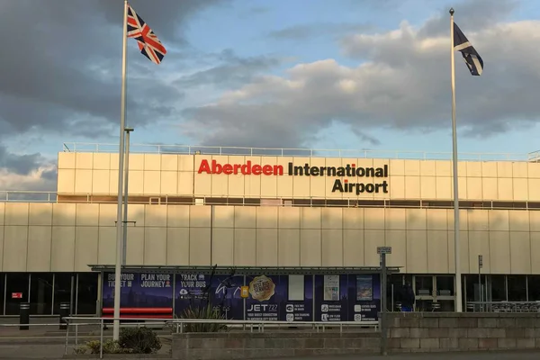 Terminal del Aeropuerto Internacional Aberdeen con banderas Union Jack y escocesas frente bajo cielo nublado.