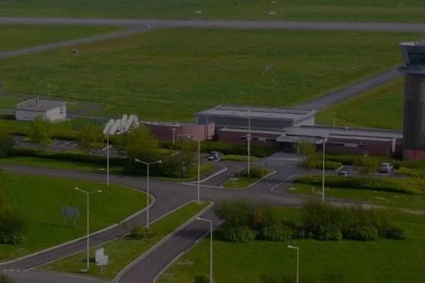 Vista aérea del Aeropuerto Amiens - Henry Potez mostrando terminal, zona de estacionamiento y campos verdes circundantes con caminos de acceso.