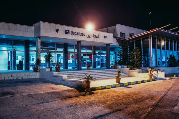 Nächtliche Ansicht der beleuchteten Abflughalle des Flughafens Amman mit blau beleuchteten Fenstern.