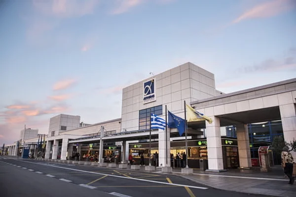 Athens Eleftherios Venizelos International Airport terminal entrance at dusk with Greek flags and modern architecture visible.