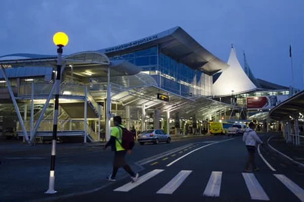 Terminal dell'Auckland Airport al tramonto con architettura moderna, tetto bianco a forma di tenda illuminato e attraversamento pedonale.