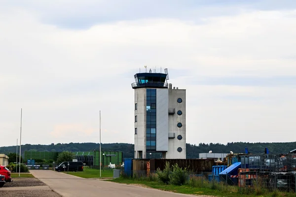 Torre de control de tráfico aéreo en Aeropuerto de Augsburgo con sección superior azul, base cilíndrica blanca y paisaje verde circundante.