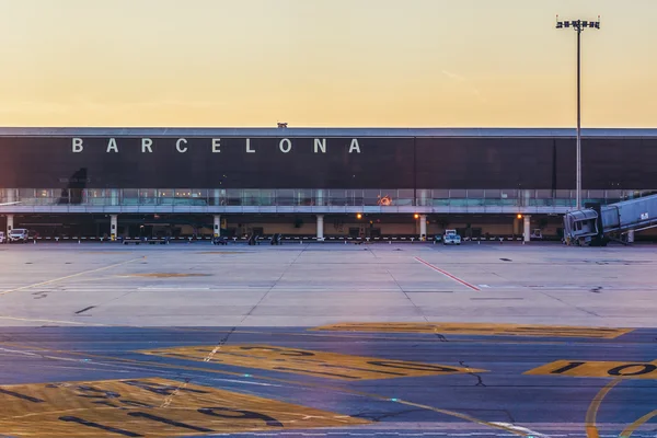 Empty tarmac at Josep Tarradellas Barcelona-El Prat Airport with the terminal building displaying "BARCELONA" signage during dawn or dusk.