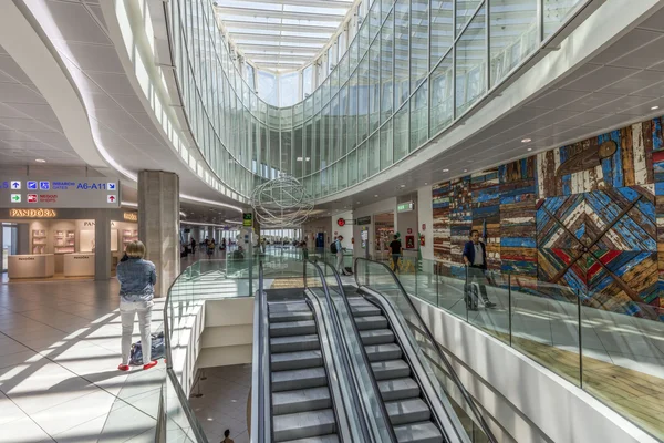 Modern interior of Bari Palese Airport terminal with escalators, glass railings, and natural skylight illuminating the contemporary architectural space.