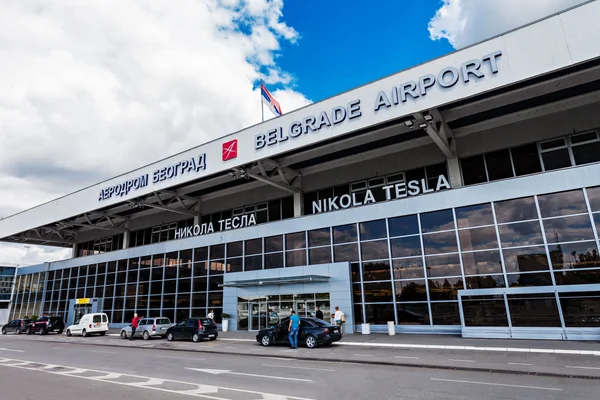 Belgrade Nikola Tesla Airport terminal building exterior with modern glass facade and signage under blue sky with clouds.