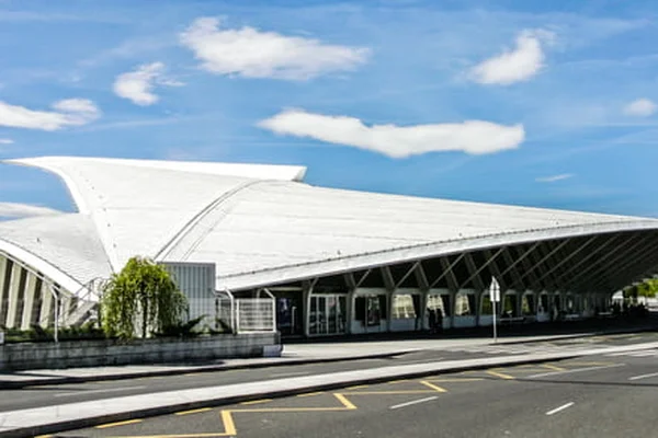 Modern white architectural terminal building of Bilbao Airport with distinctive curved roof design under blue sky with clouds.