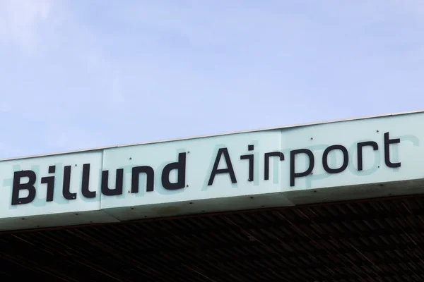 Un panneau indiquant « Aéroport de Billund » monté sur une structure de bâtiment contre un ciel bleu clair.