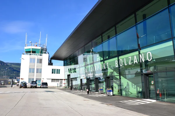 Bolzano Airport terminal building with control tower and modern glass facade under clear blue sky.