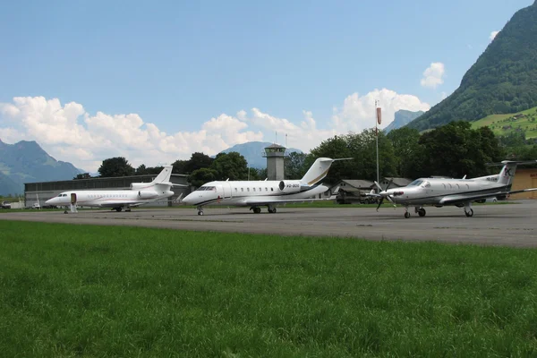 Tres aeronaves blancas estacionadas en el Aeropuerto de Buochs con montañas verdes.