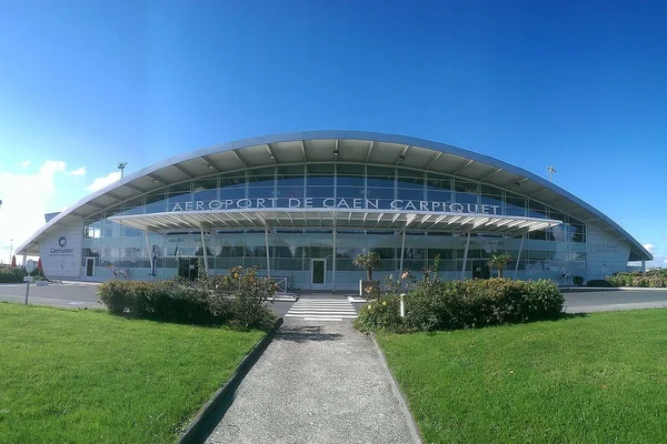 Terminal curvo moderno del Aeropuerto de Caen Carpiquet con césped verde bajo cielo azul.