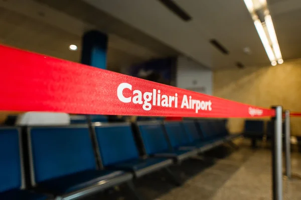 Red signage reading "Cagliari Airport" above blue seating in an airport terminal waiting area.