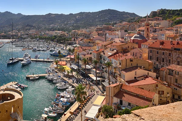 Vista aérea del puerto de Calvi con edificios terracota y montañas al fondo.