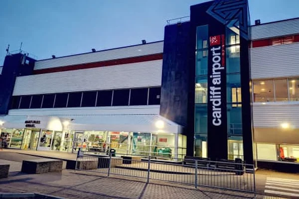 Budynek terminalu lotniska w Cardiff o zmroku z oświetlonym napisem i nowoczesną architekturą z fasadami ze szkła i metalu.