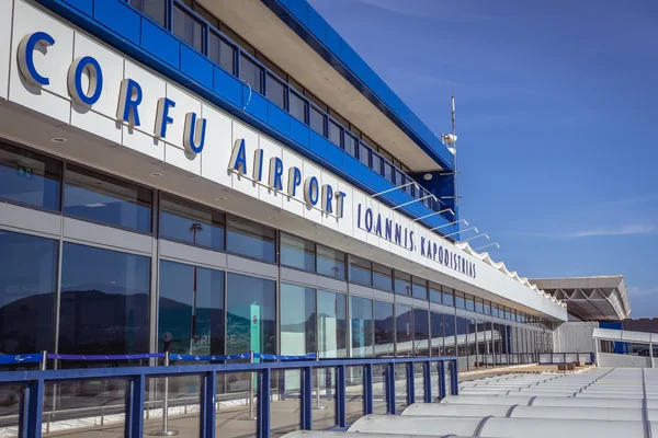 Modern terminal building of Corfu Airport "Ioannis Kapodistrias" with blue and white signage under clear sky.