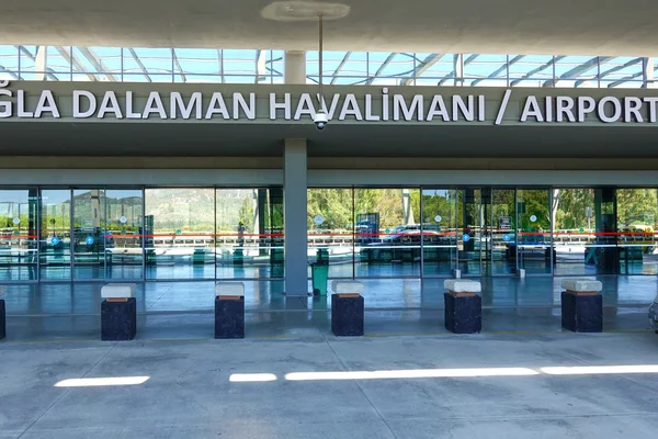 Eingang des Flughafens Dalaman mit modernen Glastüren, poliertem Boden und Beschilderung unter natürlicher Beleuchtung.