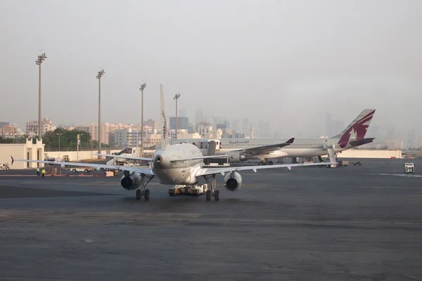 Ein Qatar Airways Flugzeug steht am Flughafen Doha International mit Stadtsilhouette im dunstigen Hintergrund.