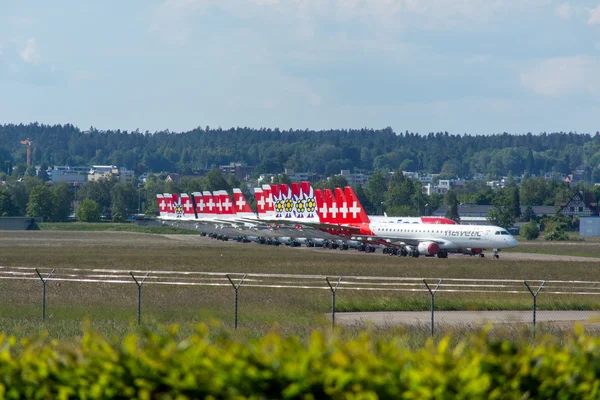 Szwajcarski samolot z namalowaną flagą zaparkowany na bazie lotniczej Dübendorf z widocznym lasistymi górami w tle.