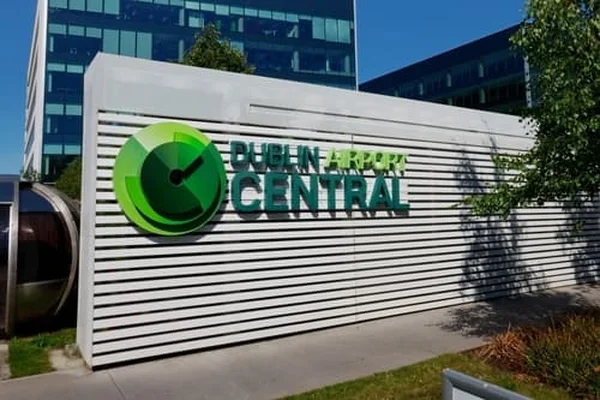 Gran letrero verde y blanco del Aeropuerto de Dublín con logo de reloj en fachada moderna.