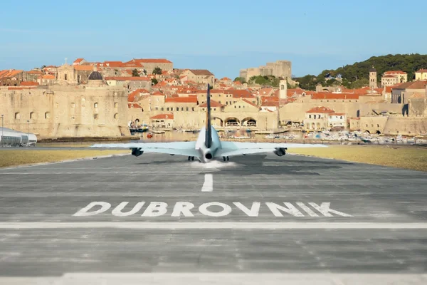A military transport aircraft lands on the runway at Dubrovnik Airport with the historic walled city of Dubrovnik visible in the background.