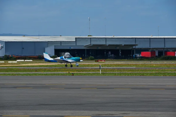 Piccolo aereo blu e bianco parcheggiato a Essendon Fields con grandi hangar sullo sfondo.