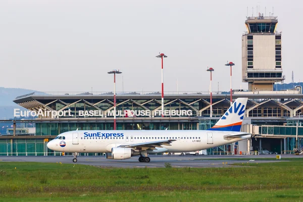 Aeronave SunExpress estacionada en el Aeropuerto EuroAirport Basel Mulhouse Freiburg con edificio terminal y torre de control visibles al fondo.