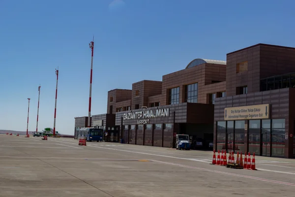 Exterior view of Gaziantep Oğuzeli Airport terminal building with brown brick architecture, flags, and tarmac during daytime.