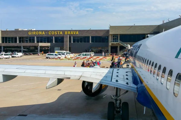 A commercial aircraft parked at Girona-Costa Brava Airport with passengers boarding via stairs, terminal building visible in background.