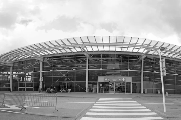 Moderno edificio terminal curvado de vidrio y metal con paso peatonal blanco en Aeropuerto Grenoble Alpes Isère bajo cielo nublado.