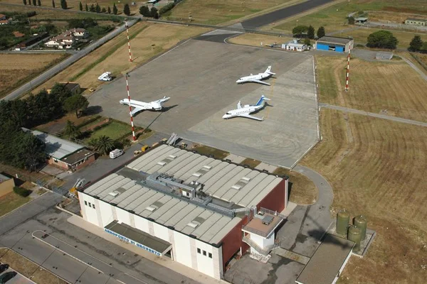 Aerial view of Grosseto Airport showing three gliders parked on the tarmac, a red and white hangar building, runway markings, and surrounding agricultural fields.