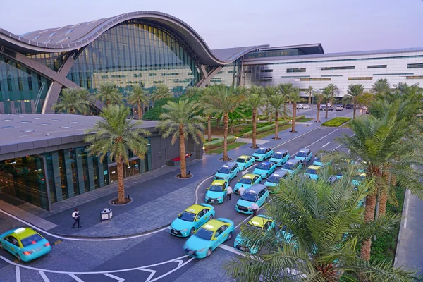 Luftaufnahme des Hamad International Airport mit moderner gekrümmter Architektur und blauen Taxis.