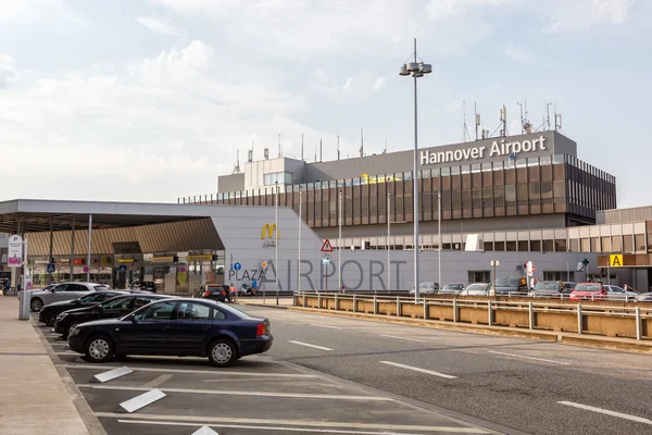 Edificio terminal del Aeropuerto de Hannover con autos estacionados en primer plano y cielo despejado encima, aeropuerto principal de Hannover, Alemania.