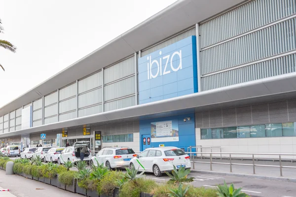 Exterior view of Ibiza Airport terminal building with blue signage, parked vehicles, and modern architecture featuring glass and metal features.