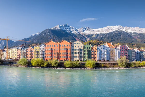 Coloridos edificios frente al agua a lo largo de un río turquesa con montañas nevadas al fondo en Innsbruck, Austria.