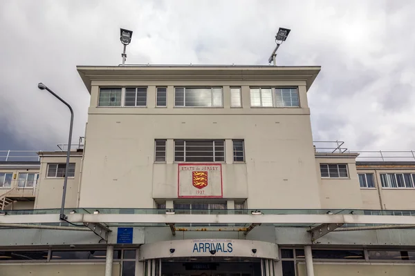 Edificio de llegadas del Aeropuerto de Jersey con fachada color crema, ventanas y emblema de escudo rojo encima de las puertas de entrada.