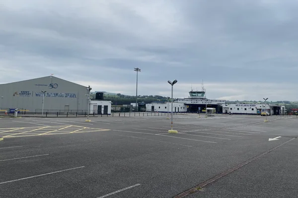 Plataforma del Aeropuerto de Kerry con hangares, torre de control e instalaciones de aeronaves bajo cielo nublado con zona de pista pavimentada.