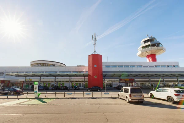 Edificio terminal del Aeropuerto de Klagenfurt con distintiva torre roja y sala de control, arquitectura moderna y vehículos estacionados bajo cielo despejado.