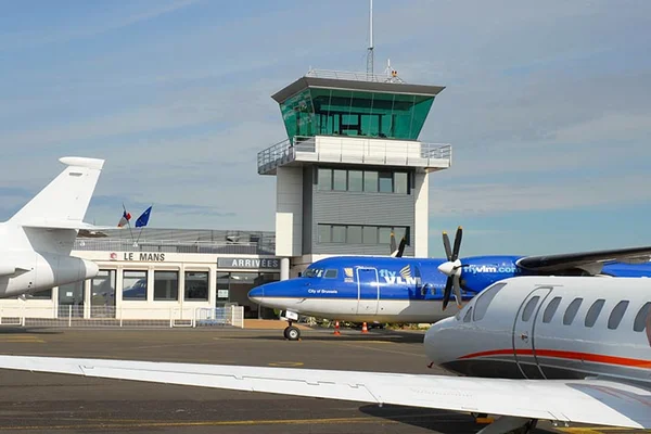 Avión azul bimotor estacionado en la terminal del Aeropuerto Le Mans Arnage con torre de control.