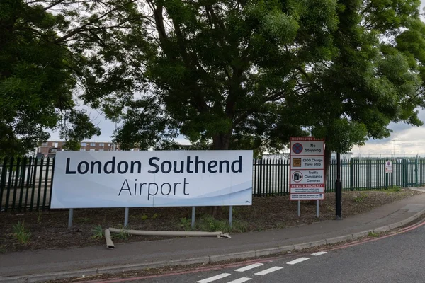 Señal blanca que lee "Aeropuerto de Londres Southend" junto a una carretera con árboles.