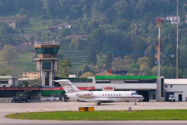 Aeropuerto de Lugano con jet privado estacionado y colinas boscosas al fondo.