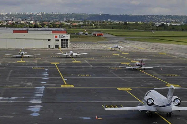 Múltiples aviones pequeños estacionados en el Aeropuerto de Lyon Bron con hangar BCA al fondo.