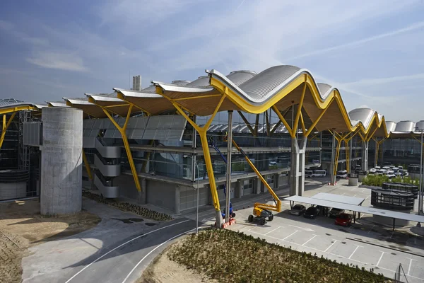 Yellow and white fabric canopy structure at Adolfo Suárez Madrid-Barajas Airport terminal with modern architecture and parking area visible.