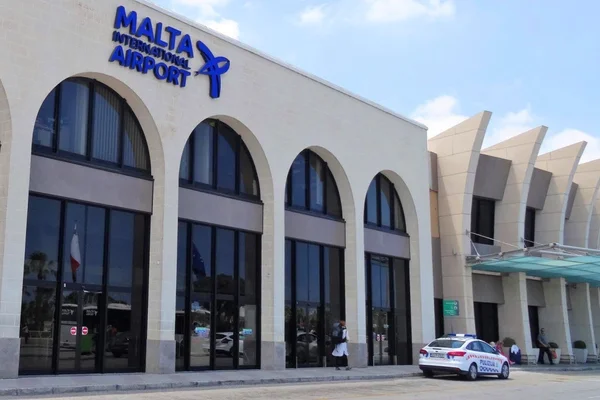 Exterior view of Malta International Airport terminal building with distinctive arched windows and modern architecture under clear sky.