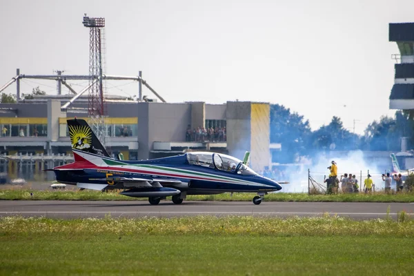 A blue aerobatic jet aircraft taxis on the runway at Maribor Edvard Rusjan Airport with ground crew and hangar buildings visible in the background.