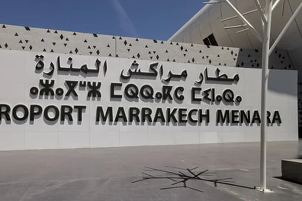 Insegna dell'Aeroporto di Marrakesh Menara su parete bianca con testo arabo e inglese.