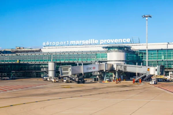 Terminal del Aeropuerto de Marsella Provenza con vehículos de servicio bajo cielo azul claro.