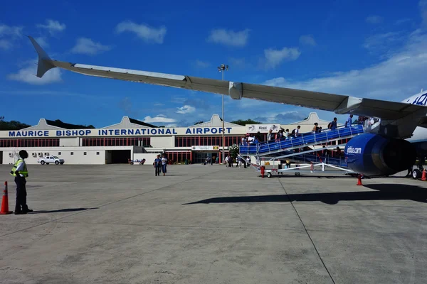 Avion bleu et blanc garé au terminal de l'aéroport Maurice Bishop avec escaliers.