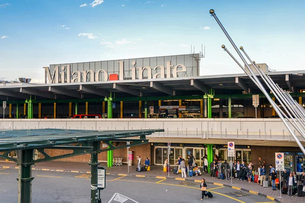 Milan Linate Airport terminal exterior with modern architecture, green structural elements, and passengers gathered outside the entrance.