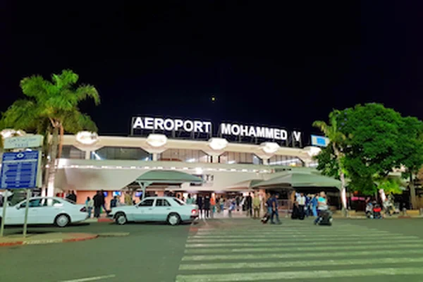 Il terminal dell'Aeroporto Internazionale Mohammed V di notte con palme e veicoli parcheggiati.